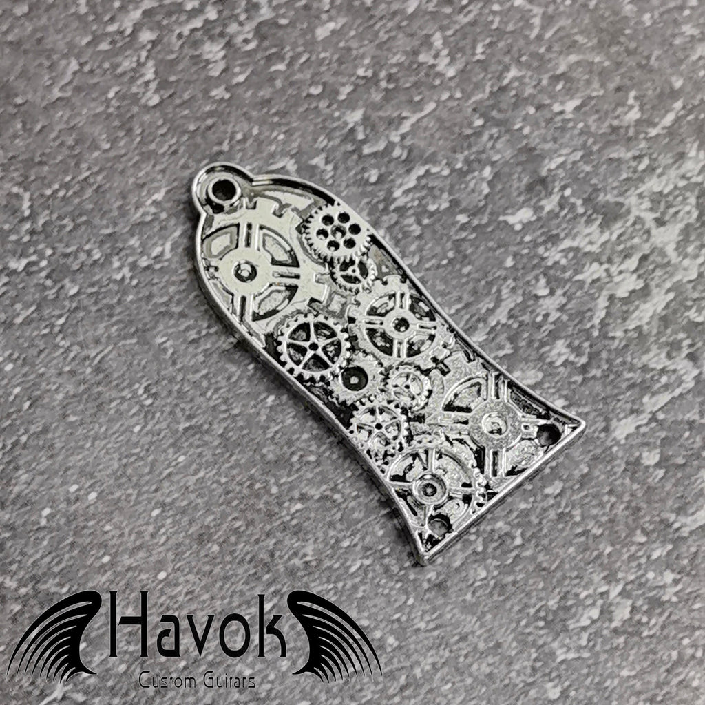 A vintage style metal truss rod plate for electric guitars. It comes in unique design of cogwheels. The color is silver.